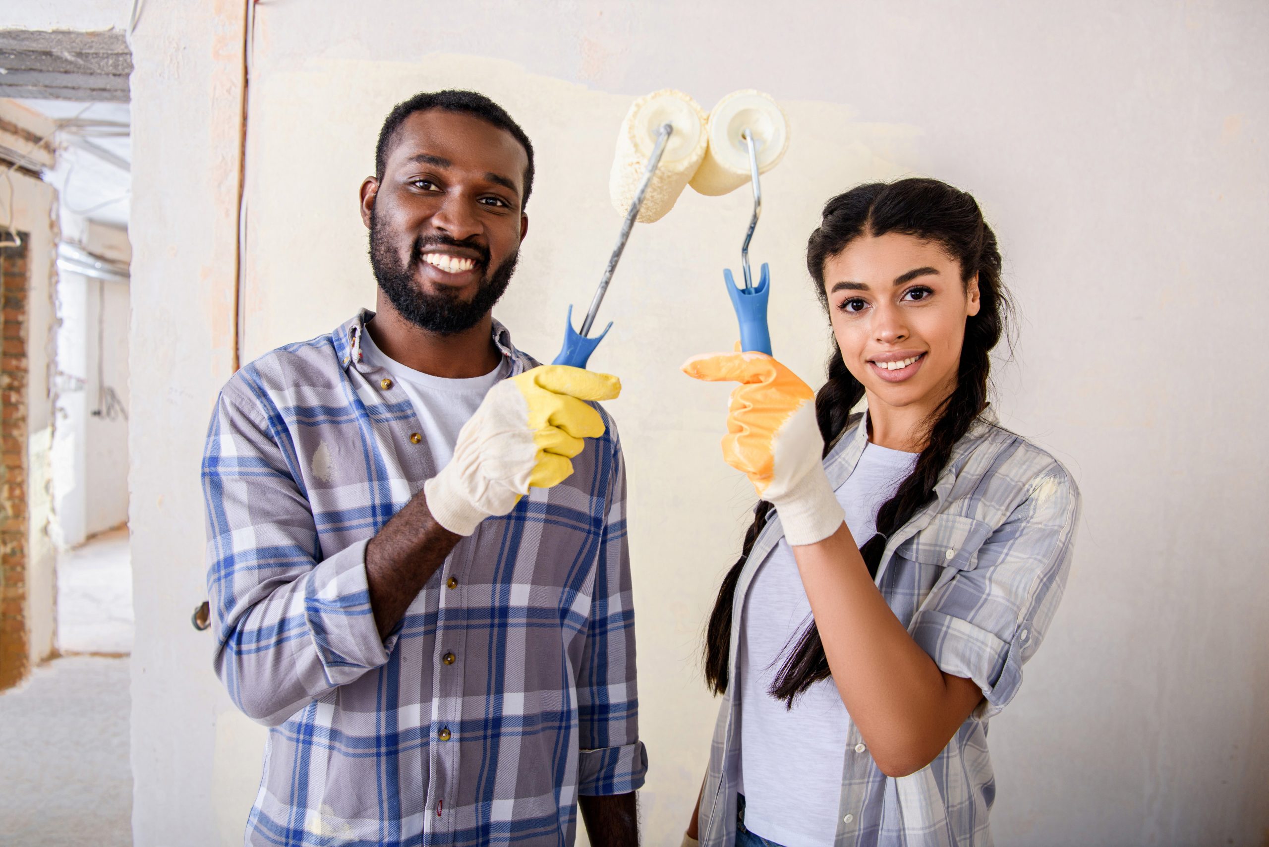 cheerful african american couple holding paint rollers and looking at camera during renovation at Importance of home maintenance - young couple looking after their home.