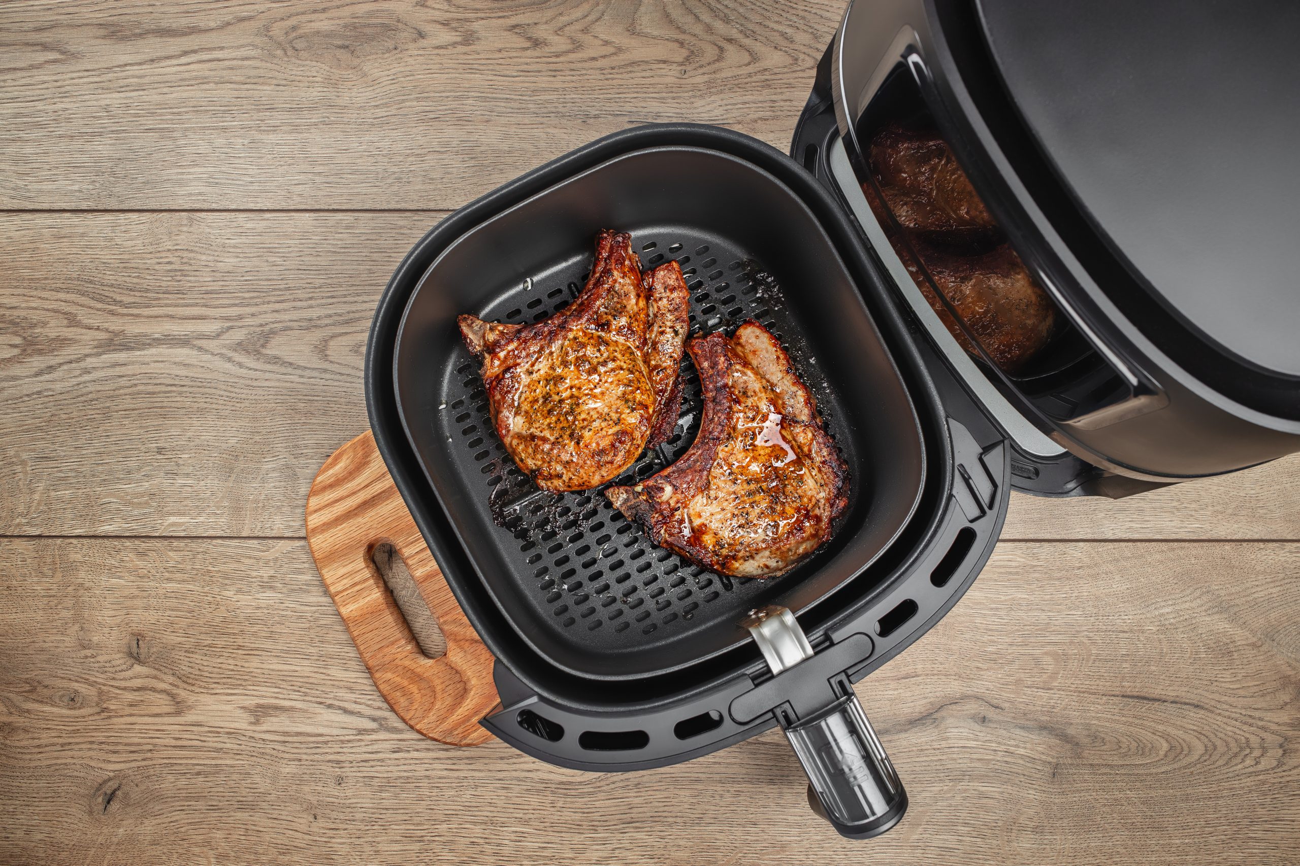 grilled steaks from air fryer oven on a wooden background, easy crispy food with little or no fat by circulating hot air inside the basket air fryer cooked grilled steaks - accompanying article about air fryer fire